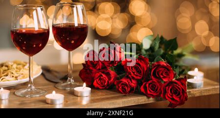 Rose, due bicchieri di vino rosso e candele alla scrivania Foto Stock