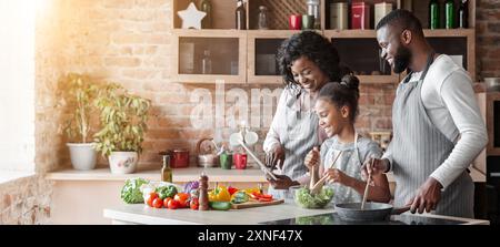 Mamma, papa' e figlia leggono la ricetta sul tablet in cucina Foto Stock