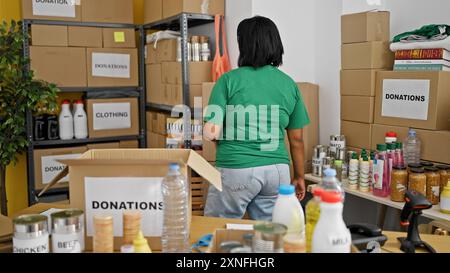 Una donna che organizza donazioni all'interno di un magazzino pieno di provviste e scatole di cartone. Foto Stock