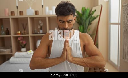 Un giovane che meditava in una sala spa con scaffali in legno e piante per creare un'atmosfera serena Foto Stock