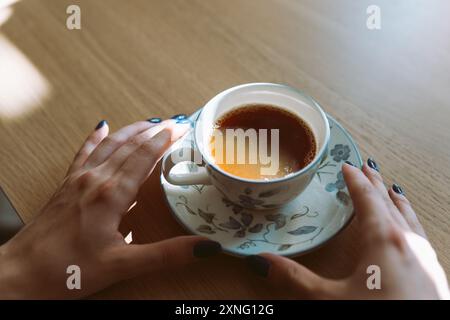 mani giovane donna che tiene la tazza sul piattino con tè verde Foto Stock