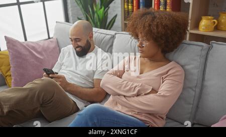 Coppia interrazziale che si rilassa su un divano, donna che sembra disinteressata mentre l'uomo ride al suo telefono Foto Stock