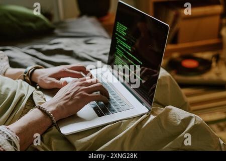 Codice a mano maschile irriconoscibile tramite moderno computer portatile seduto sul letto in una camera accogliente Foto Stock