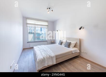 Camera da letto con letto matrimoniale king size, pavimento in legno e finestra sullo sfondo. Casa. Di giorno Foto Stock