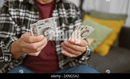 Un uomo maturo a casa che tiene sterline britanniche, che significa pianificazione finanziaria o budget in un comodo salotto. Foto Stock