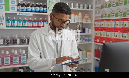 Farmacista afroamericano in camice bianco che usa una tavoletta digitale all'interno di una farmacia moderna Foto Stock