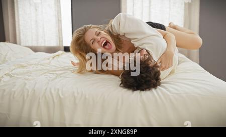Una donna e un uomo esprimono gioia mentre interagiscono giocosamente su un letto in una camera da letto luminosa. Foto Stock