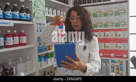 Una donna matura farmacista esamina i farmaci mentre utilizza una compressa in una farmacia moderna Foto Stock