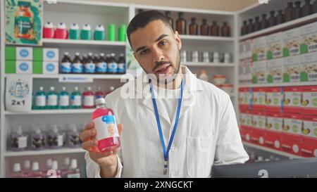 Un giovane farmacista ispanico che tiene in mano una bottiglia di farmaci si trova in una farmacia ben fornita Foto Stock