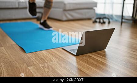 Uomo adulto che si esercita a casa con un laptop su un tappetino per yoga in un ampio soggiorno Foto Stock