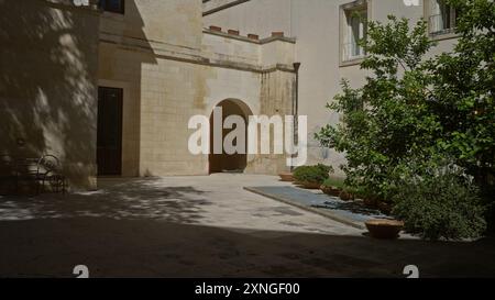 Cortile illuminato dal sole con pareti in pietra a lecce, puglia, italia, con piante verdi, una piccola panchina, e aree ombreggiate che creano un'atmosfera tranquilla all'aperto Foto Stock