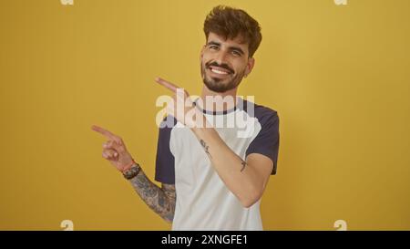 Sorridente giovane barbuto con tatuaggi rivolti verso l'alto mentre si trova contro un muro giallo. Foto Stock