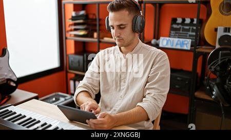 Giovane ispanico con le cuffie che usa il tablet in uno studio musicale Foto Stock