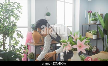 Un giovane asiatico organizza fiori in un negozio interno luminoso e pieno di verde. Foto Stock