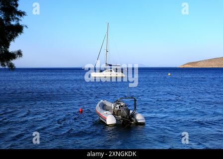 Piccolo dingy di gomma ormeggiato in acque poco profonde, con piccolo yacht in lontananza, Livadia, Isola di Tilos, Dodecaneso, Grecia. Presa nel giugno 2024 Foto Stock