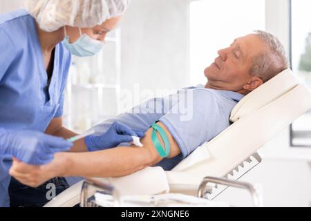 Uomo anziano sdraiato sul divano, che viene iniettato per via endovenosa in studio medico Foto Stock