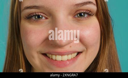 Foto ravvicinata di una ragazza allegra e gioiosa sorridente, isolata sullo sfondo blu dello studio. Ritratto di un adolescente allegro e allegro, con un'espressione facciale positiva Foto Stock