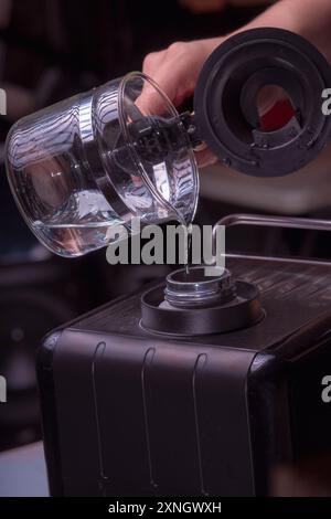 Woman Barista gestisce una macchina per preparare un caffè delizioso, primo piano di mani per preparare un caffè espresso, versando acqua per preparare il caffè. Foto Stock