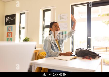 Al liceo, adolescente che alza la mano in classe, partecipando a una lezione Foto Stock