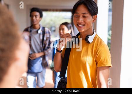 Gli adolescenti del corridoio delle scuole superiori sorridono e parlano con gli amici, indossando le cuffie Foto Stock