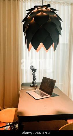 Spazio di lavoro creativo con microfono e laptop sotto una lampada elegante. Perfetto per podcasting, creazione di contenuti e temi home Office. Foto Stock