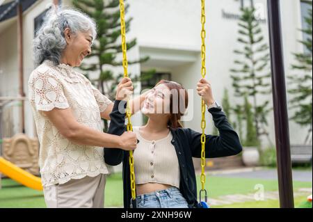 Una nonna asiatica felice e positiva sta parlando e toccando delicatamente i capelli di sua nipote mentre riposa nel suo giardino di casa. La nipote sì Foto Stock