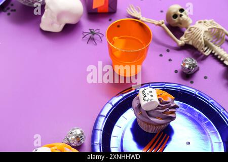 Tavolo da festa di Halloween con cupcake, drink e scheletro su sfondo viola Foto Stock