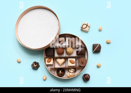 Scatola con deliziose caramelle al cioccolato e noci su sfondo blu Foto Stock