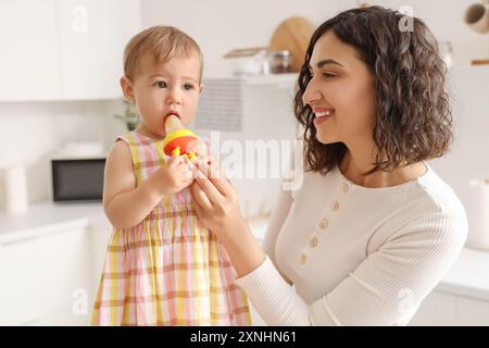 Madre che dà alla sua piccola rosticceria con il cibo in cucina Foto Stock