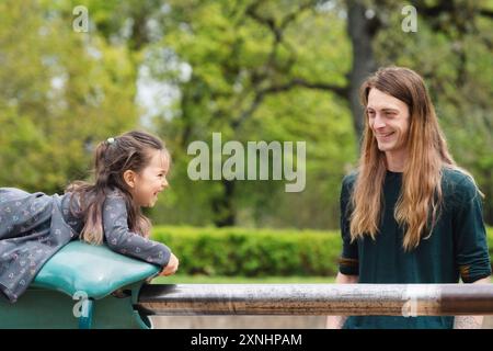 un padre sorridente guarda sua figlia giocare su uno scivolo in un parco Foto Stock