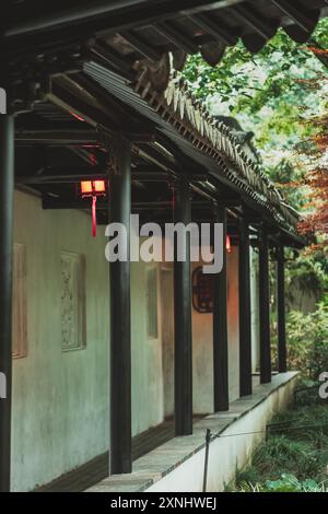 Un tradizionale giardino cinese con un passaggio coperto, fiancheggiato da colonne e caratterizzato da lanterne rosse. Foto Stock