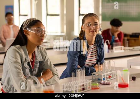 Al liceo, ragazze adolescenti che indossano occhiali di sicurezza frequentano un corso di chimica Foto Stock