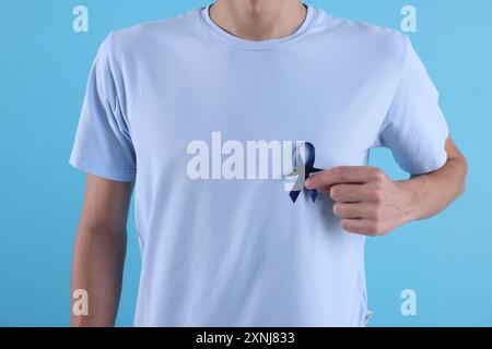 Consapevolezza del cancro alla prostata. Uomo con nastro blu e baffi finti su sfondo colorato, primo piano Foto Stock