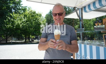 Un uomo tiene in mano un cono gelato con una cannuccia. Sta sorridendo e si sta godendo la sua sorpresa Foto Stock
