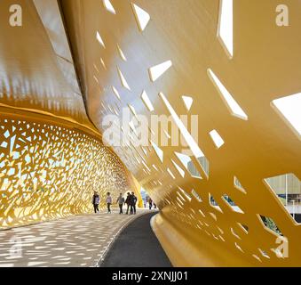 Tettoia forata di bicicletta e ponte pedonale. Swansea Arena e Copr Bay Bridge, Swansea, Regno Unito. Architetto: acme, 2024. Foto Stock