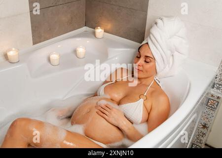 Donna incinta che si gode un bagno di bolle Foto Stock