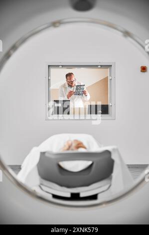 Tomografia computerizzata medica o scanner RM. Medico che esamina i risultati della risonanza magnetica in clinica. Specialista maschile che indossa occhiali e uniforme, tiene la scansione, studia. Concetto di medicina e ospedale. Foto Stock