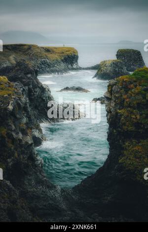 Piccola persona umana solitaria, escursionista sul bordo delle scogliere dell'Oceano Atlantico ad Arnastapi, in Islanda, in una giornata buia e tempestosa Foto Stock