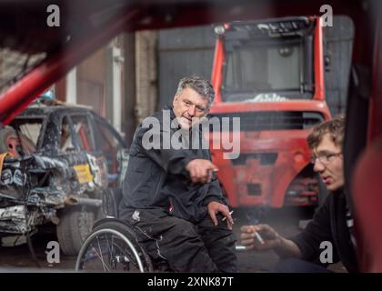 Gli adolescenti apportano le modifiche finali sulle auto di scorta con la guida di un mentore in sedia a rotelle in un'officina di Brandeburgo. Una metafora per superare le sfide e il lavoro di squadra. Foto Stock