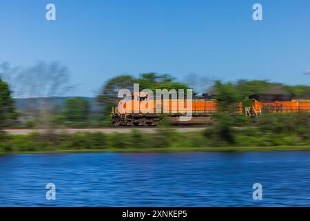 Locomotive ferroviarie che accelerano lungo i binari lungo un fiume. Foto Stock