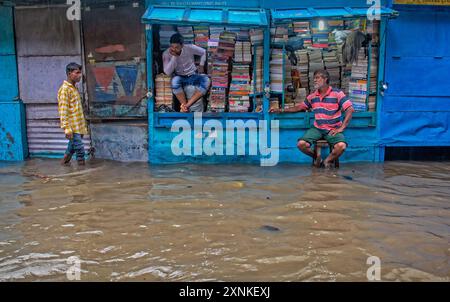 I venditori di libri siedono in una stalla inondata a Kolkata, in India, mentre un uomo cammina attraverso la strada bagnata dopo una forte pioggia. Foto Stock