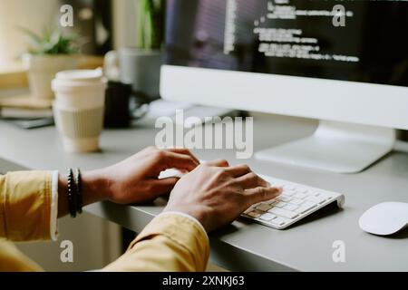 Primo piano medio delle mani di un programmatore maschio irriconoscibile che digita il codice su un computer desktop in un ufficio moderno Foto Stock
