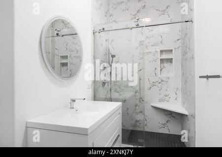 Un bagno con armadio bianco e lavabo console, rubinetto cromato e soffione doccia, marmo bianco e doccia con piastrelle quadrate nere. Foto Stock