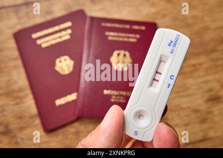 Augusta, Baviera, Germania - 1 agosto 2024: Hand tiene il test COVID-19 positivo accanto a due passaporti. Immagine simbolica cancellazione delle vacanze estive pianificate a causa di una malattia da coronavirus in estate. FOTOMONTAGGIO *** mano hält positiven COVID-19 test neben zwei Reisepässen. Symbolbild Absage des geplanten Sommerurlaub aufgrund einer Coronavirus Erkrankung im Sommer. FOTOMONTAGE Foto Stock