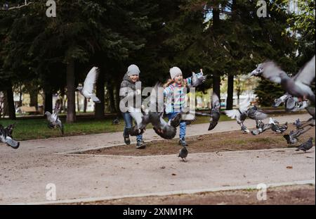 bambini che corrono nel parco a caccia di piccioni. Concetto di infanzia felice e spensierata. Foto Stock