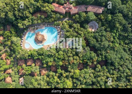 Paesaggio tropicale con tetti delle ville e piscina blu tra palme verdi vista aerea dei droni Foto Stock