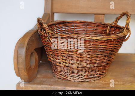 Vecchio cestino di vimini su una panca di legno. Cestino di paglia nella cucina del cottage. Vita di campagna. Foto Stock