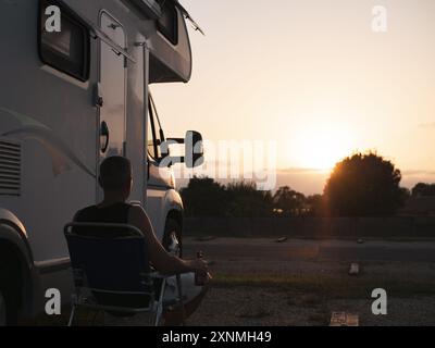 Uomo seduto fuori dal suo camper a bere una birra e a guardare il tramonto Foto Stock