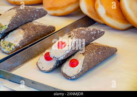 Cannolo siciiano di pasta dolce fatta in casa ripieno di mandorle, pistacchio, limone, vaniglia, crema al cioccolato sul mercato alimentare italiano Foto Stock