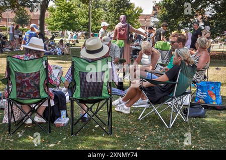 Persone sedute nel parco su sedie pieghevoli godendosi il tempo estivo inglese. Inghilterra Regno Unito Foto Stock